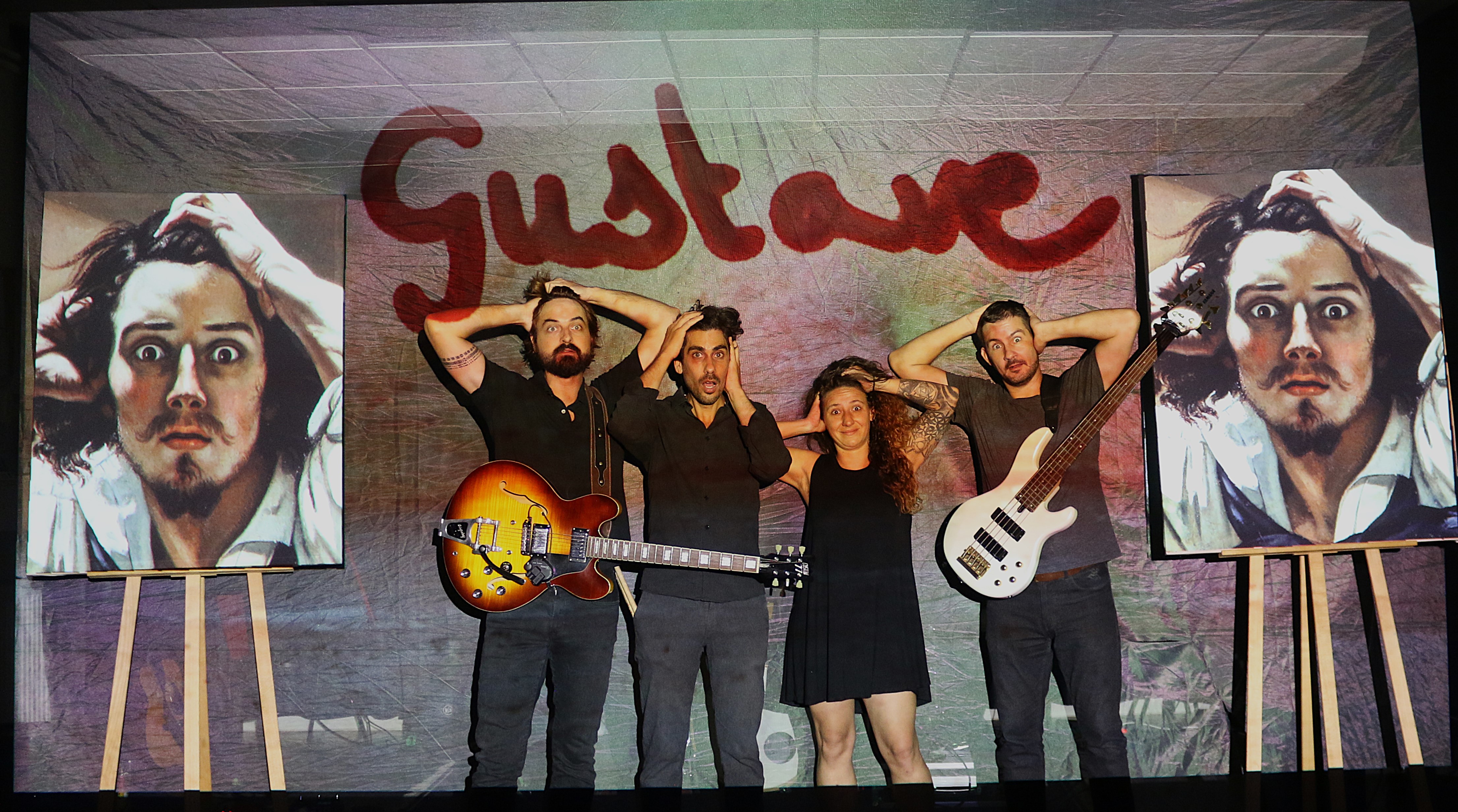 Les quatre artistes de Gustave sur scène, devant une toile où le mot Gustave est peint en rouge.